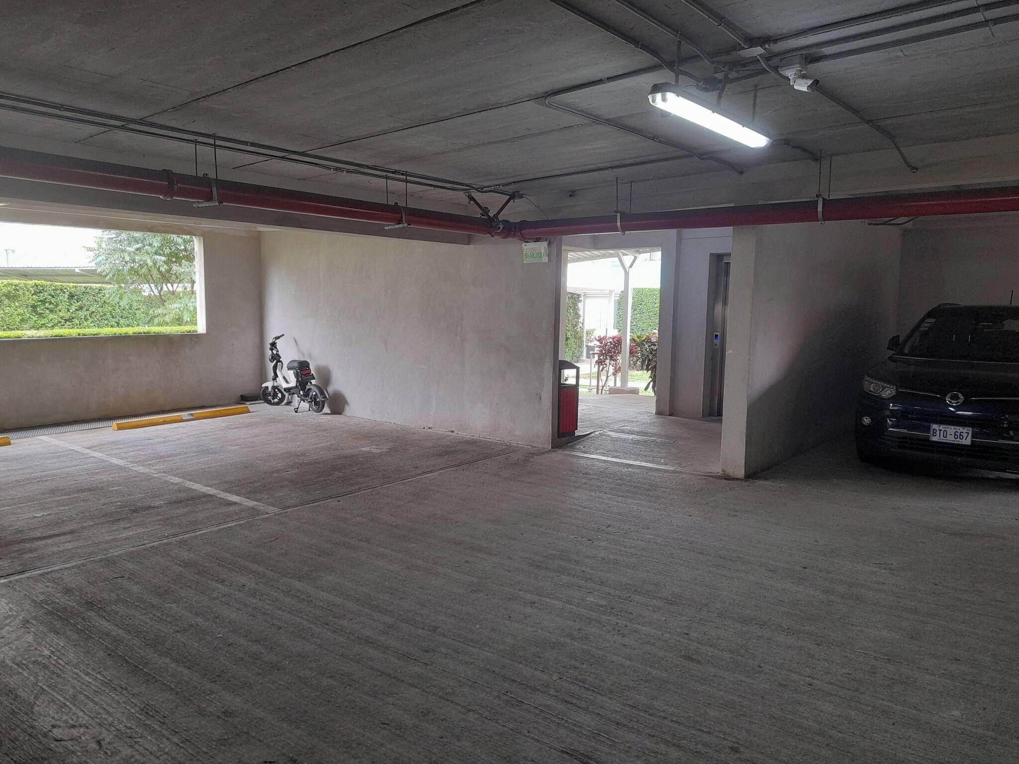 A parking garage with a concrete floor, a scooter, and a car.