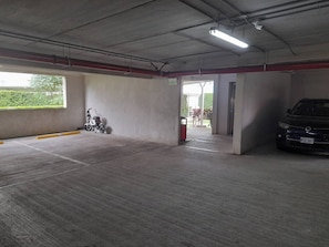 A parking garage with a concrete floor, a scooter, and a car.