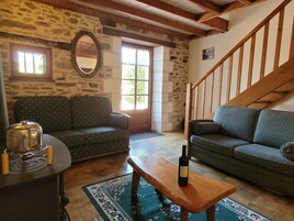 Una sala de estar acogedora con una pared de piedra, dos sofás, una mesa de madera con una botella y una escalera.