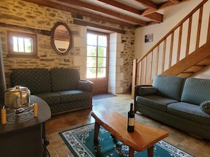 A cozy living room with a stone wall, two sofas, a wooden table with a bottle, and a staircase. - Charming and Spacious Gite With Shared Pool (Saint-Saud-Lacoussiere)