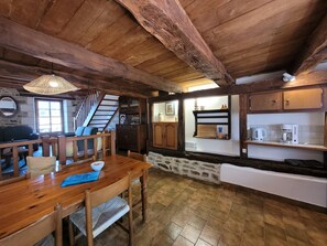 A rustic interior with a wooden dining table, chairs, a staircase, and a kitchen area with cabinets and a sink. - Charming and Spacious Gite With Shared Pool (Saint-Saud-Lacoussiere)