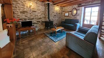 A cozy living room with stone walls, a fireplace, a sofa, a television, and a wooden ceiling.