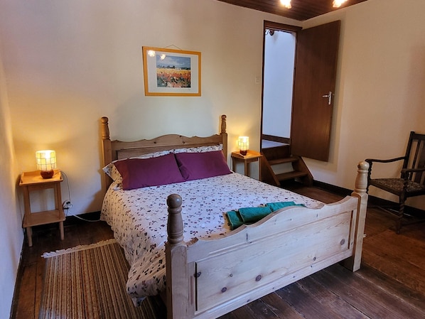 A wooden bed with a headboard, two bedside tables with lamps, a framed picture on the wall, and a door. - Charming and Spacious Gite With Shared Pool (Saint-Saud-Lacoussiere)