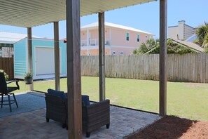 Ein überdachter Patio-Bereich mit Gartenmöbeln, einem Holzzaun und Blick auf ein Wohngebäude im Hintergrund.