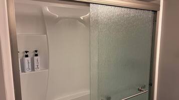 A bathroom with a shower enclosure, a glass door, and two bottles of shampoo on a shelf.