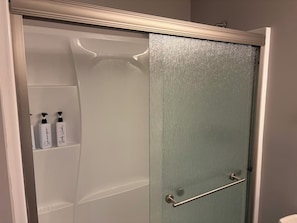 Un bagno con cabina doccia, porta in vetro e due flaconi di shampoo su uno scaffale.