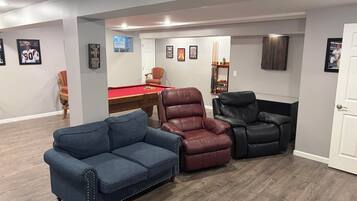 A room with a pool table, two leather chairs, and a blue sofa.