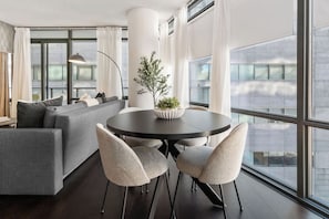 A modern living room with a round table, two chairs, a sofa, and a potted plant.