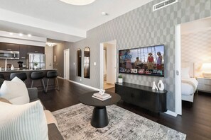 Een moderne woonkamer met een ronde salontafel, een flatscreen televisie aan de wand, en een keuken op de achtergrond.