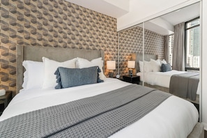 A hotel room with a large bed, a nightstand with a lamp, a mirror, and a patterned wall.