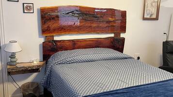 A bedroom with a wooden headboard, a bedside table with a lamp, a trash bin, and a chair.