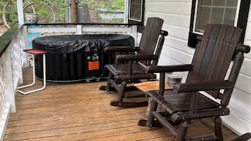 Een overdekt terras met houten vloer, twee schommelstoelen, een barbecue en een hangplanter.