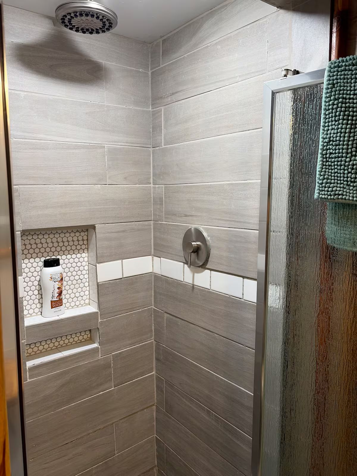 Een douche met een regendouche, een handdoekhouder en een plank met toiletartikelen.