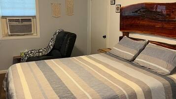 Une chambre à coucher comprenant un lit, une chaise, un ventilateur de plafond et un climatiseur fixé au mur.