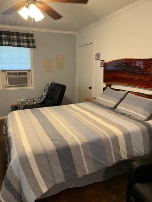 A bedroom with a bed, a chair, a ceiling fan, and a wall-mounted air conditioner.
