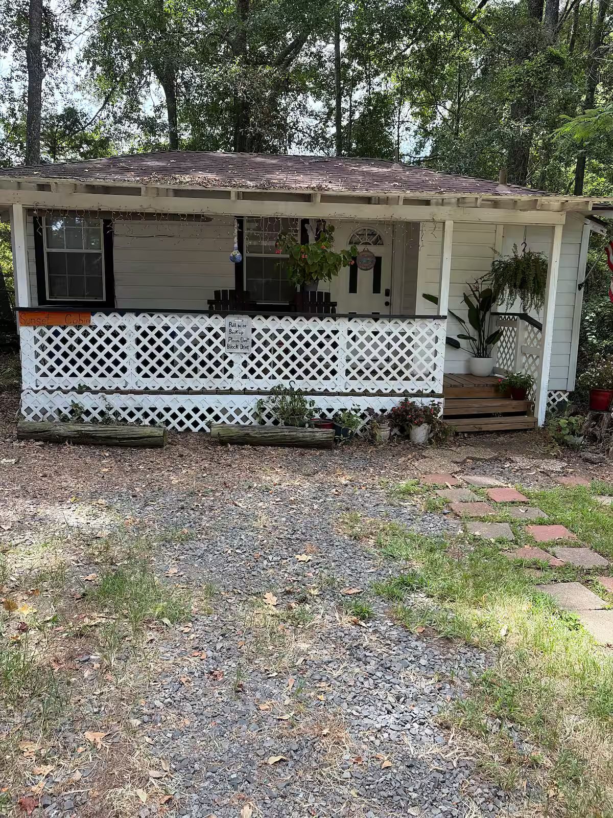 A single-story house with a porch, a small deck, and a gravel driveway.