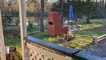 A wooden deck with a lattice railing, a brick structure, and a blue umbrella in a wooded area.
