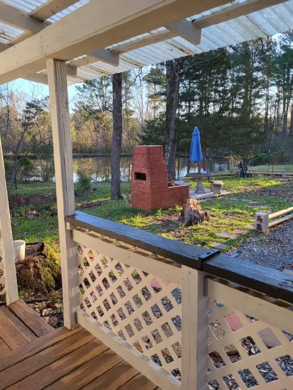 A wooden deck with a lattice railing, a brick structure, and a blue umbrella in a wooded area.
