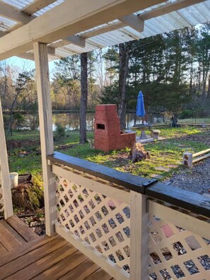 Une terrasse en bois avec une balustrade en treillis, une structure en briques et un parasol bleu, le tout situé dans un espace boisé.