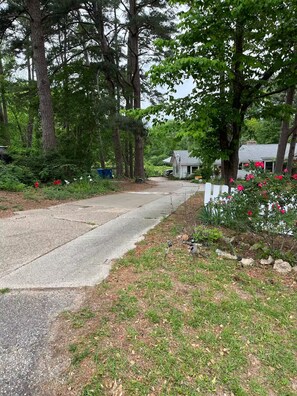 A residential street with a sidewalk, a house with a flag, and a garden with flowers. - Sunset Cabin (Marshall)