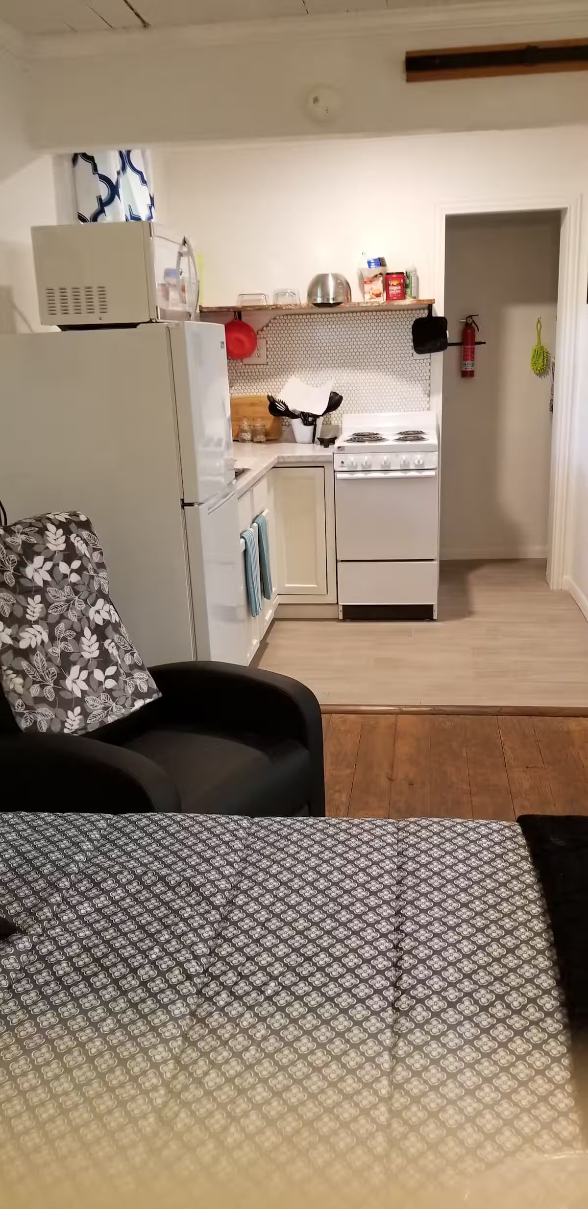 Een ruimtelijke zithoek met een kitchenette, een bank en een vloerkleed met een patroon.