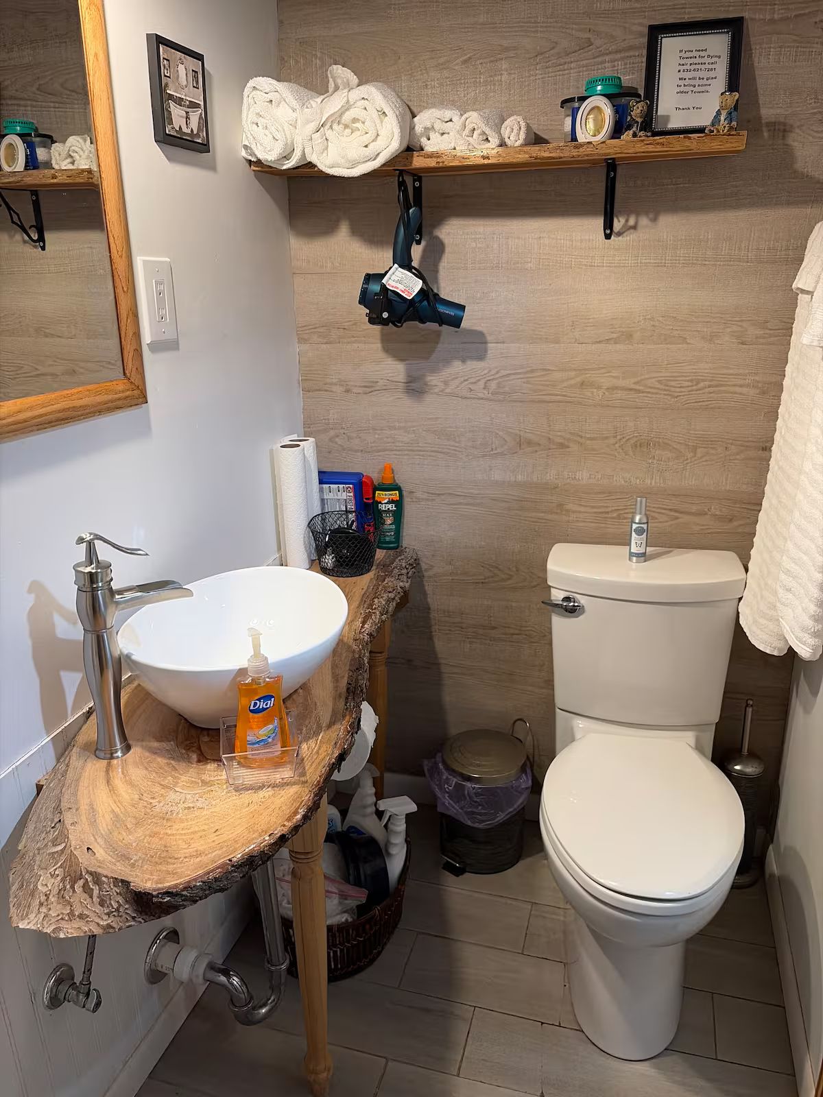 Een badkamer met een houten wastafelmeubel, een wastafel, een toilet en planken met handdoeken en toiletartikelen.