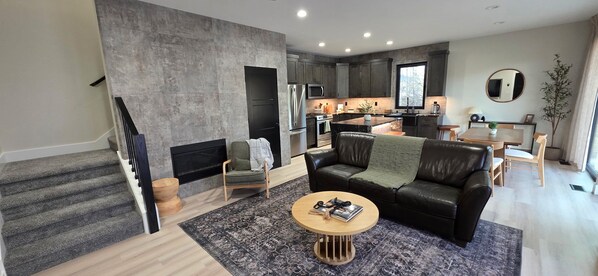 A modern living room with a fireplace, a leather sofa, and a dining area with a table and chairs.