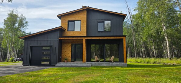 A modern two-story house with a garage, large windows, and a porch with chairs.