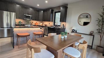 A modern kitchen with dark cabinets, stainless steel appliances, and a wooden dining table with chairs.
