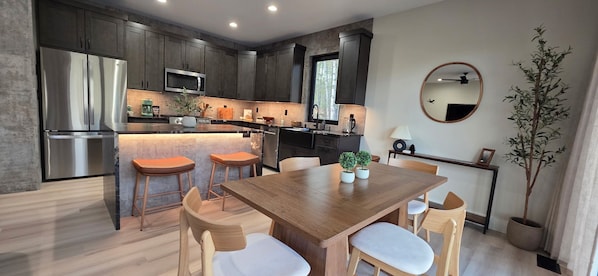 A modern kitchen with dark cabinets, stainless steel appliances, and a wooden dining table with chairs.