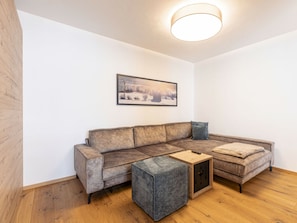 Un salon moderne avec un canapé d’angle, un petit pouf et un tableau encadré au mur.