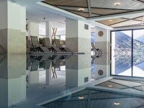 Un intérieur moderne avec un sol réfléchissant, un coin salon avec des fauteuils et une grande fenêtre offrant une vue sur les montagnes.