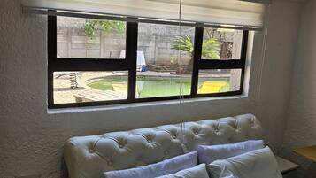 A bedroom with a large window, a tufted headboard, and a view of an outdoor swimming pool.