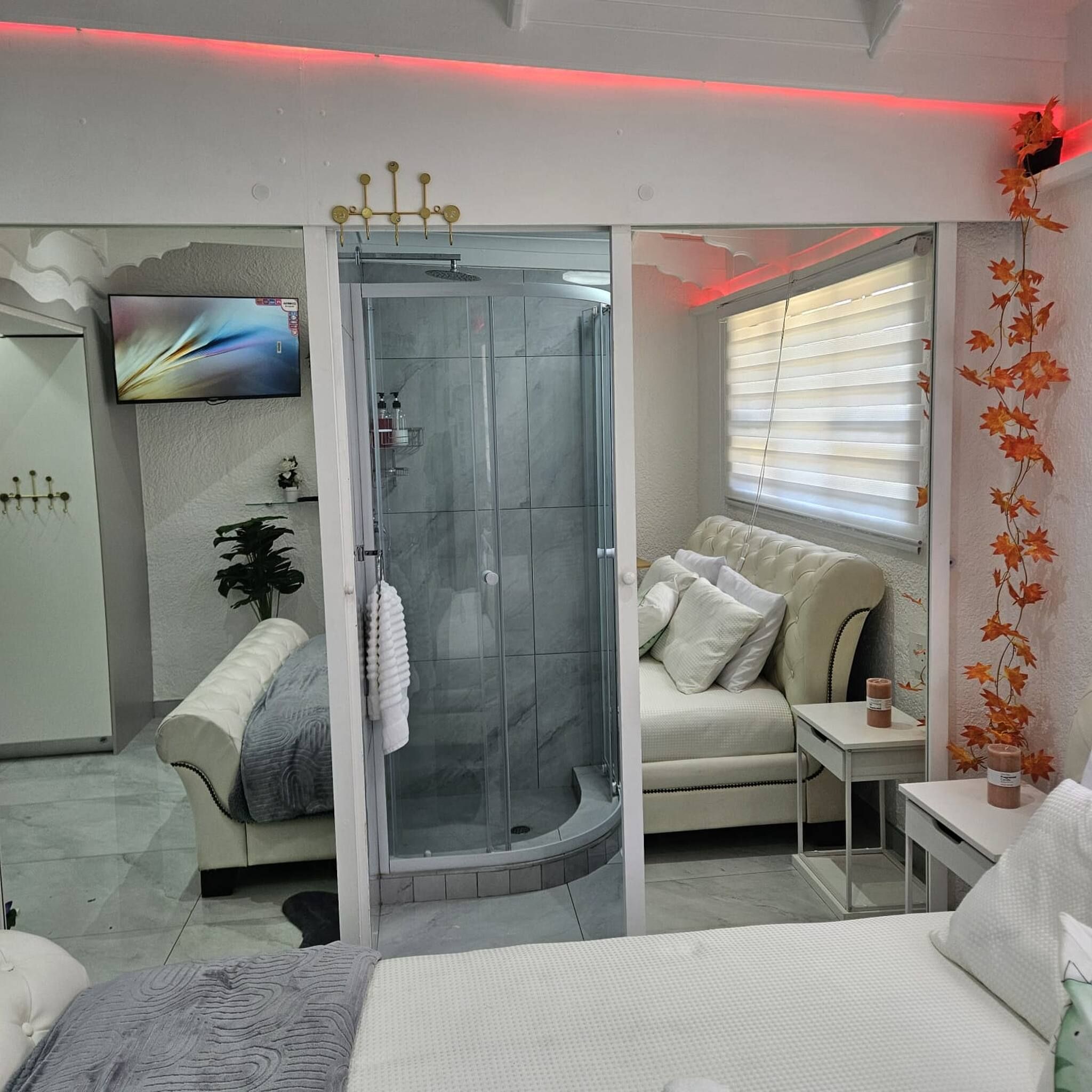 A modern bathroom with a glass shower enclosure, a white vanity, and a flat-screen TV mounted on the wall.