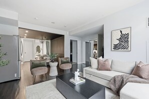 A modern living room with a sofa, coffee table, and a dining area with a table and chairs. - 3BR/3BA Downtown Toronto + Free Parking | Parking Available (Toronto)