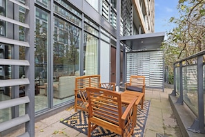 Een terras met een tafel en stoelen, omgeven door grote ramen en uitzicht op de stad.