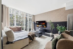 A modern living room with a sofa, a coffee table, a TV mounted on the wall, and a fireplace. - 3BR/3BA Downtown Toronto + Free Parking | Parking Available (Toronto)