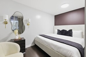 A modern hotel room with a large bed, a bedside table, a chair, and a mirror. - 3BR/3BA Downtown Toronto + Free Parking | Parking Available (Toronto)