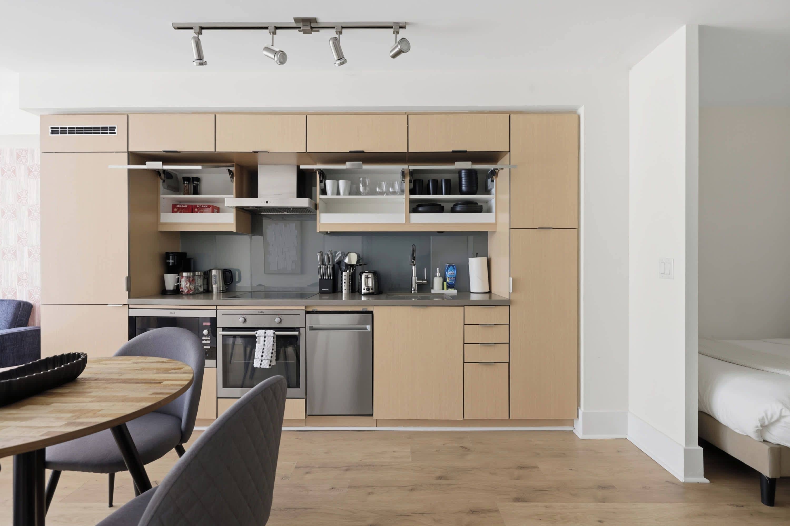 Cozinha moderna com eletrodomésticos integrados, sala de jantar com mesa e cadeiras, e uma cama no quarto adjacente.