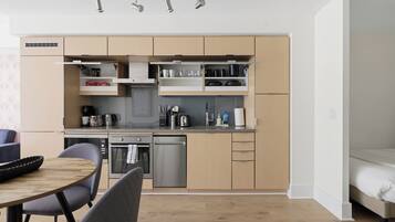 Cozinha moderna com eletrodomésticos integrados, sala de jantar com mesa e cadeiras, e uma cama no quarto adjacente.