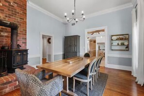Een eetgedeelte met een houten tafel en stoelen, een bakstenen muur, een zwarte kookplaat en een kroonluchter.