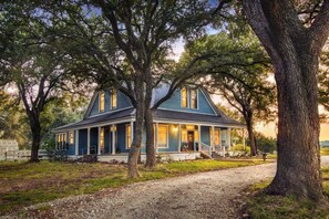 A two-story house with a porch, surrounded by trees.