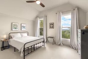 Een slaapkamer met een bed, een nachtkastje, een dressoir, een raam met gordijnen en een plafondventilator.