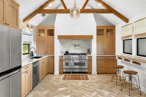 A kitchen with wooden cabinets, stainless steel appliances, a herringbone floor, and a hanging light fixture.