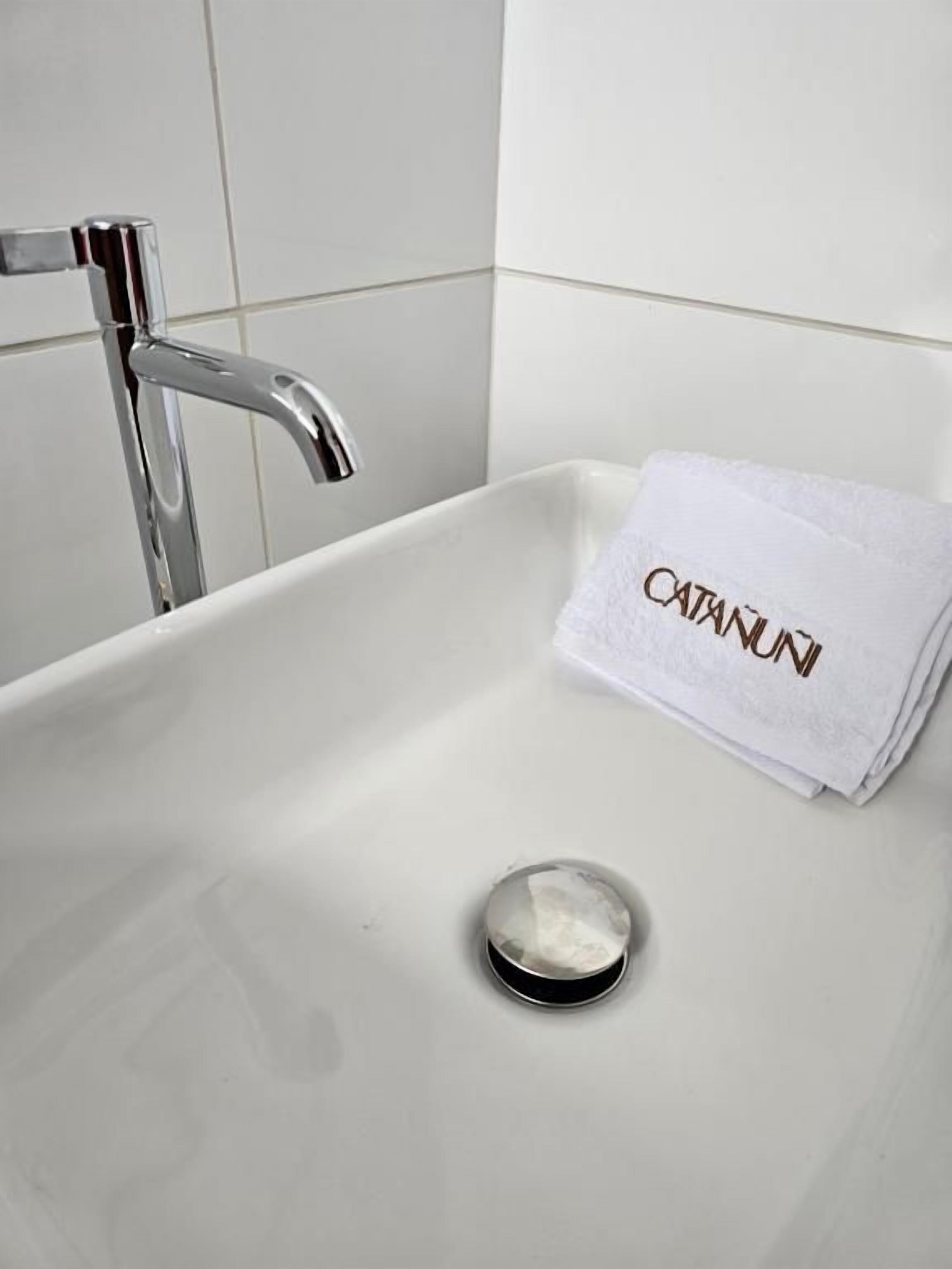 Une salle de bain avec un lavabo blanc, un robinet chromé et une serviette ornée du texte « CATANUI ».