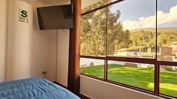 Un dormitorio con cama, televisor en la pared y un amplio ventanal con vistas a un paisaje verde.