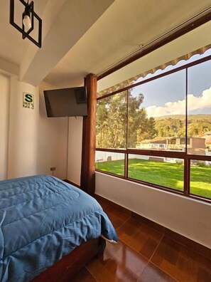 A bedroom with a bed, a television on the wall, and a large window with a view of a green landscape. - Hotel Catañuñi  (Sapallanga)