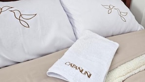 A bed with a white pillow featuring a leaf design, a white towel with 'CATANUNI' text, and a beige blanket with a white trim. - Hotel Catañuñi  (Huancayo)