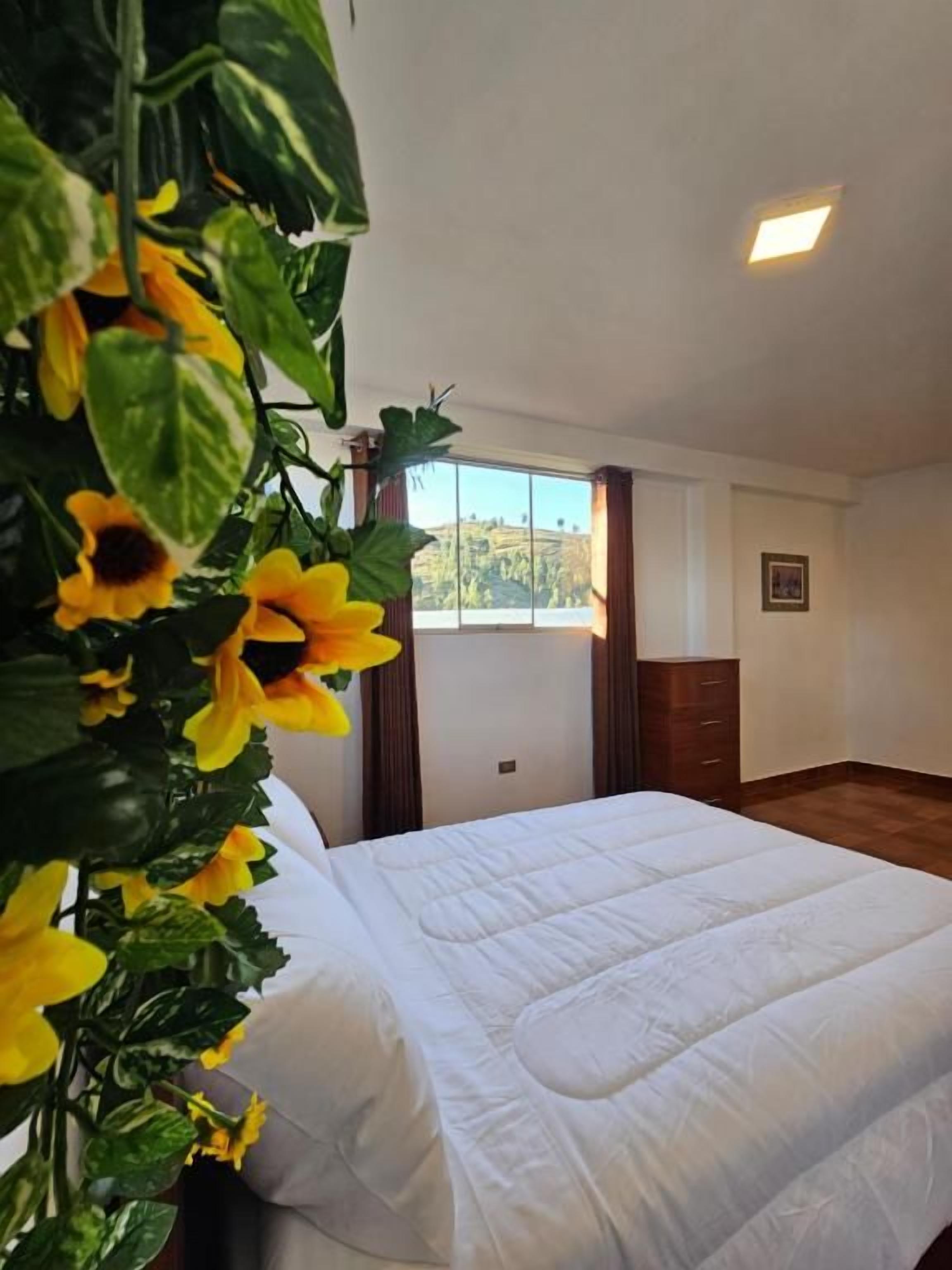 Ein Schlafzimmer mit einem Bett, einem Fenster und einer Pflanze mit gelben Blüten.