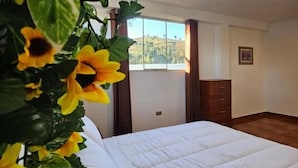 A bedroom with a bed, a window, and a plant with yellow flowers. - Hotel Catañuñi  (Huancayo)